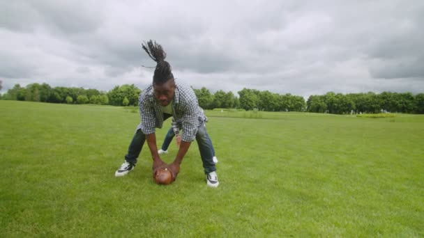 Lystig, svart, liten sønn og far som leker amerikansk fotball utendørs – stockvideo