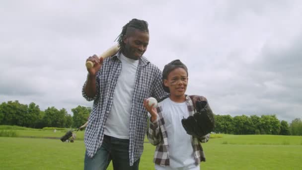 Positiv afrikansk pappa och son går på plan efter baseball match — Stockvideo