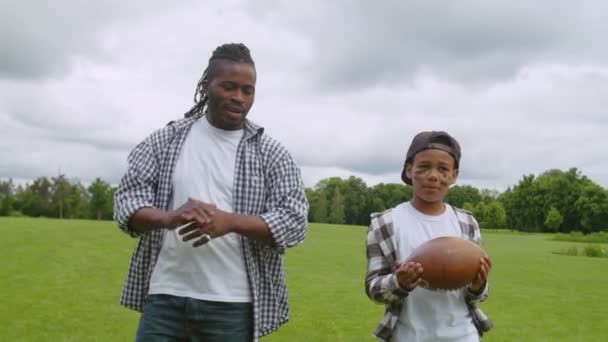 Feliz papá africano y el niño de la escuela caminando en el campo para jugar fútbol americano — Vídeos de Stock