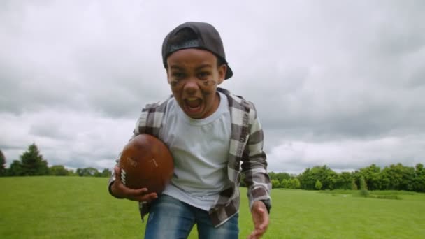 Overexcited little african boy with american football running on field — Stock Video