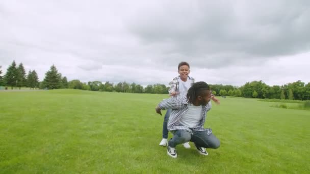 Despreocupado negro papá piggybacking alegre hijo en la naturaleza — Vídeos de Stock