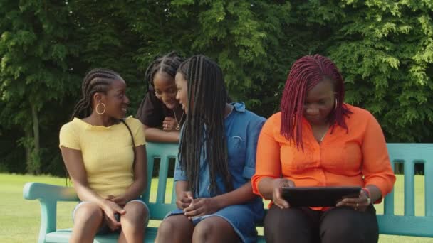 Cheerful pretty african sisters chatting while mom networking on tablet pc in park — Stock Video