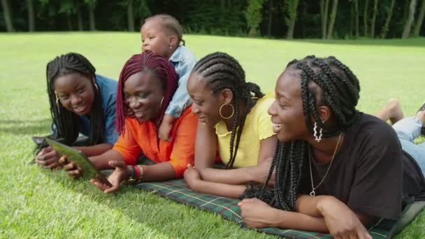 Χαρούμενη μαύρη οικογένεια ξαπλωμένη στο καρό και μοιράζονται tablet PC στο πάρκο — Αρχείο Βίντεο