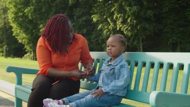 Заботливая черная мама и прекрасная маленькая дочь сближаются на открытом воздухе — стоковое видео