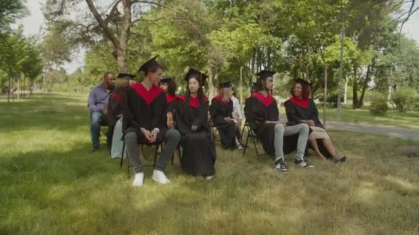 Grupo de estudantes multiétnicos diversos em vestidos acadêmicos no dia de formatura — Vídeo de Stock