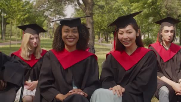 Smiling multiethnic female students in academic dresses expressing happiness outdoors — Stock Video