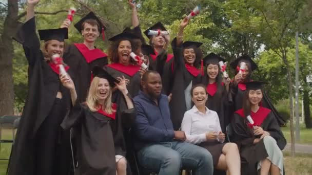 Excitados graduados multiétnicos con diplomas y personal académico celebrando el día de la graduación — Vídeos de Stock