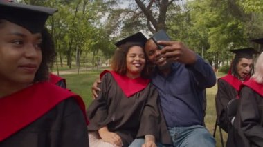 Mezuniyet elbisesi içinde mezuniyet gününde selfie çeken mutlu siyah baba ve kız.