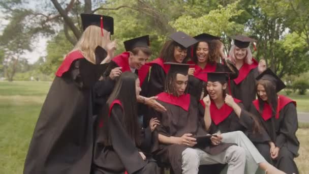 Diplômés multiraciaux joyeux en robes universitaires travaillant sur tablette PC après la cérémonie de remise des diplômes — Video