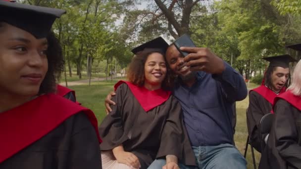 Ευτυχισμένος μαύρος μπαμπάς και η κόρη στο φόρεμα αποφοίτησης λαμβάνοντας selfie στην ημέρα αποφοίτησης — Αρχείο Βίντεο