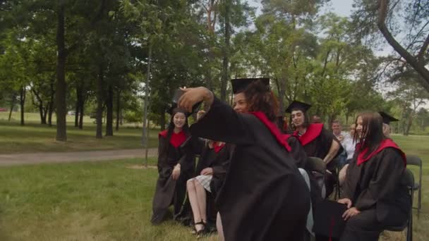 Skupina radostných rozmanitých multietnických absolventů nahrávání videa na telefonu v den promoce — Stock video