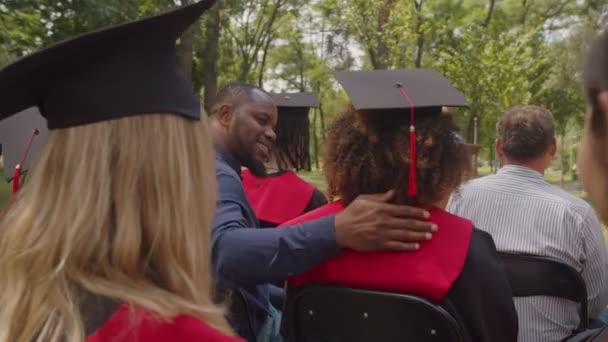 Διαφορετικοί περήφανοι γονείς αγκαλιάζουν πολυφυλετικούς αποφοίτους στην τελετή αποφοίτησης — Αρχείο Βίντεο