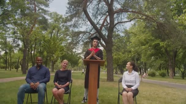 Vidám férfi arab diplomás beszédet tart diáktársaival a diplomaosztó napján — Stock videók
