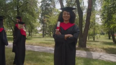 Gülümseyen Afro-Amerikan kadın diploması ile açık havada poz veriyor.