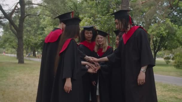 Veselý rozmanité multiraciální absolventi v maturitní šaty a malty stohování ruce venku — Stock video