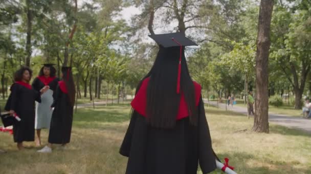 Zadní pohled na veselou absolventku s diplomem kráčející ve veřejném parku — Stock video