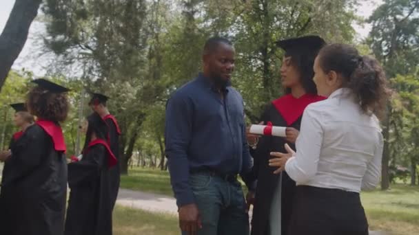 Pós-graduação africana positiva comunicando com professores universitários no dia da formatura — Vídeo de Stock