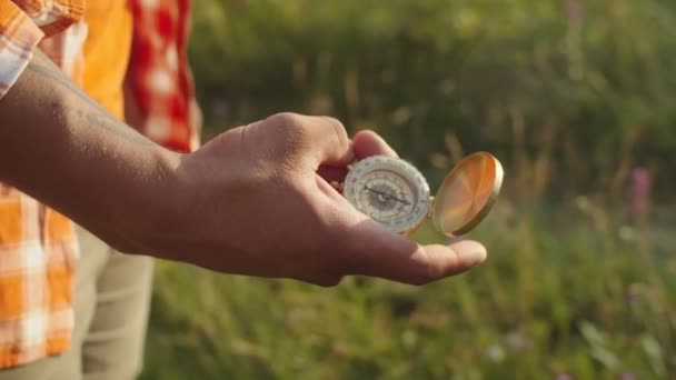 Zwarte mannelijke hand met magnetisch kompas voor navigatie buitenshuis bij zonsondergang — Stockvideo