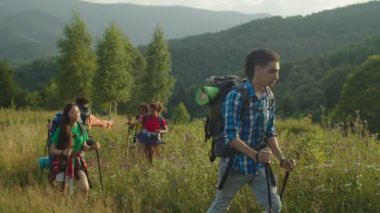 Gün batımında tepeye tırmanan sırıklara sahip çeşitli etnik çeşitlilikte gezginler.