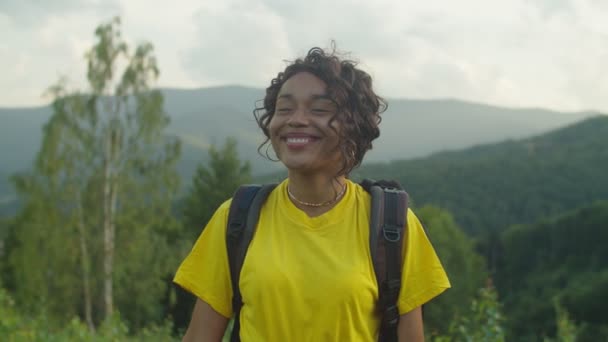 Portret van een gelukkige Afrikaanse vrouw wandelaar glimlachend over het schilderachtige berglandschap bij zonsondergang — Stockvideo