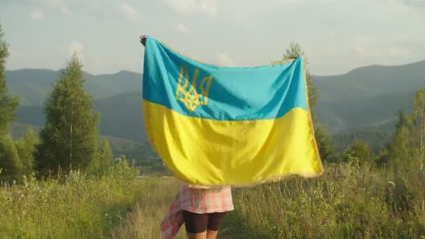 Feliz bonita hembra negra con la bandera de Ucrania de pie en la cima de la montaña al atardecer — Vídeos de Stock