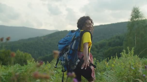 Mooie zwarte vrouwelijke wandelaar wandelen op bergweide en strekkende hand vragen om te volgen — Stockvideo