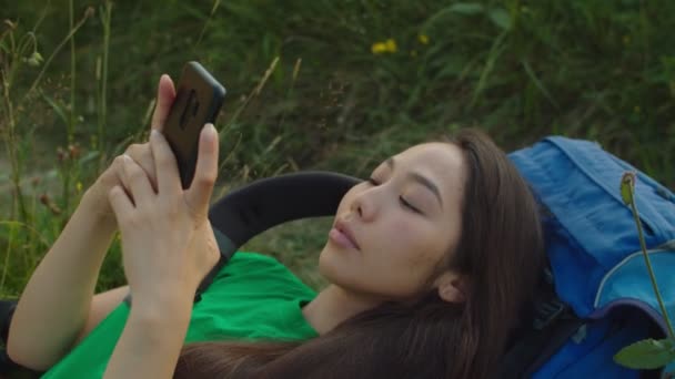 Porträtt av ganska asiatisk kvinnlig backpacker med mobiltelefon på bergstoppen vid solnedgången — Stockvideo