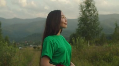 Güzel, pozitif Asyalı kadın gün batımında manzaralı dağ manzarasında gülümsüyor.