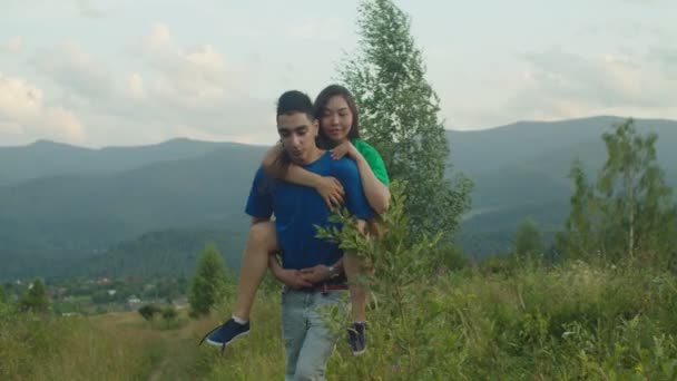 Беззаботный араб, подпирающий радостную возбуждённую азиатскую подружку в горах — стоковое видео