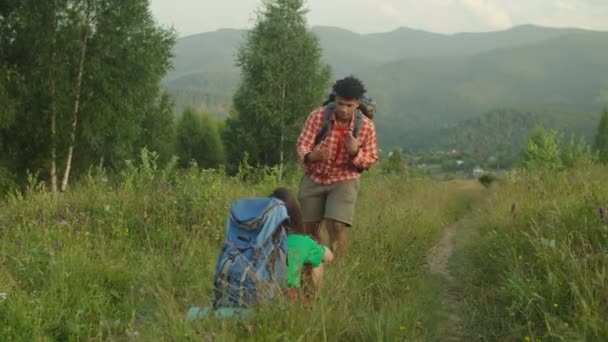 Cuidar africano senderista masculino ayudar a mujer asiática viajero a ponerse de pie fuera del suelo en la caminata — Vídeos de Stock