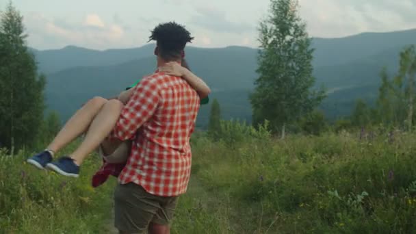 Романтичный черный мужчина с возбужденной азиаткой на руках и кружащейся на горном холме — стоковое видео