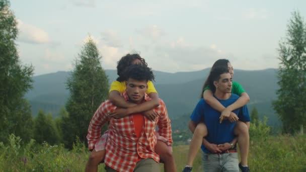 Felices excursionistas masculinos multiétnicos apoyando a alegres mujeres bonitas en el sendero de montaña al atardecer — Vídeos de Stock