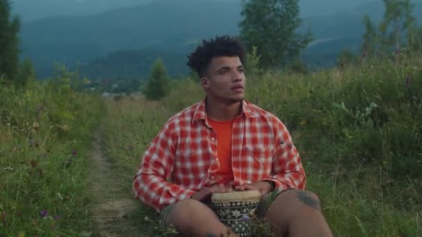 Snygg hipster afrikansk man spelar djembe trumma på berg kulle vid solnedgången — Stockvideo