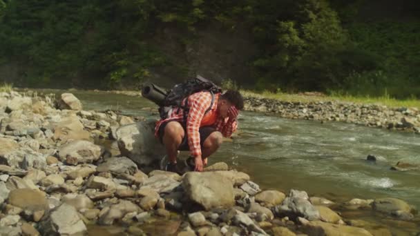 Hombre africano guapo viajero salpicaduras de agua en las manos mientras se lava la cara con agua del río de montaña — Vídeo de stock