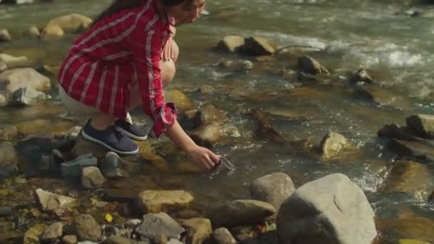 Lovely cheerful asian woman hiker filling travel mug with cold fresh water from mountain river — Stock Video