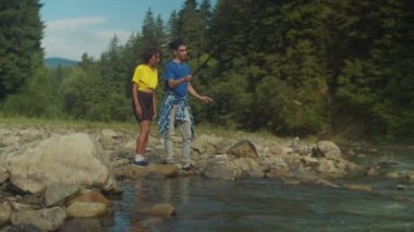 Olumlu Arap adam, güzel Afro-Amerikan kadınına dağ nehrinde balık tutmayı öğretiyor.