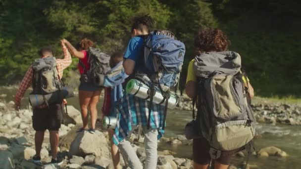 Achteraanzicht van diverse multiraciale toeristen met rugzakken rugzak per bergrivier — Stockvideo