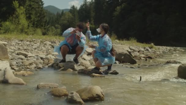 Různí multietničtí vědci v ochranných uniformách zkoumají vzorky vody ze znečištěné horské řeky — Stock video