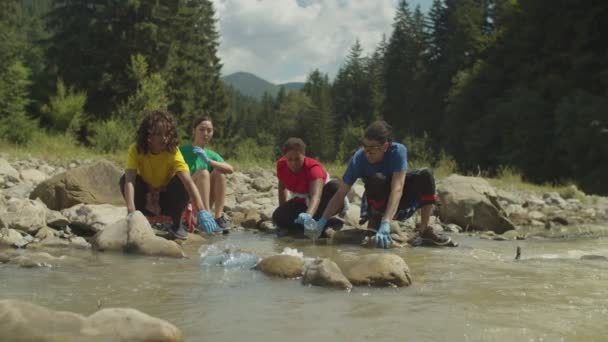 Различные мультиэтнические эко-волонтеры, очищающие горные реки от пластиковых отходов — стоковое видео