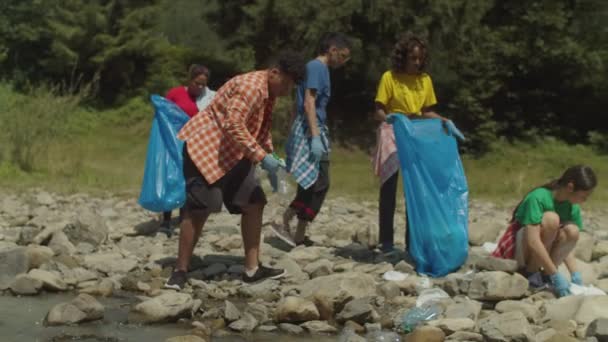 Écologistes multiraciaux emballant les déchets plastiques dans des sacs poubelles pendant le nettoyage de l'environnement — Video