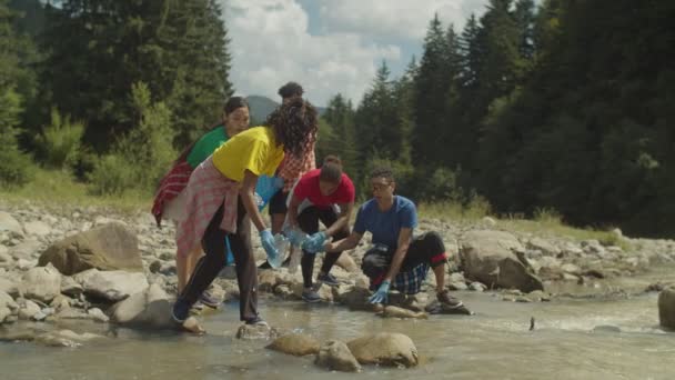 Ecologicamente consciente de diversas pessoas multiétnicas fazendo limpeza ambiental no rio de montanha — Vídeo de Stock