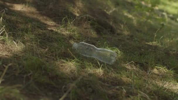 Nahaufnahme einer schwarzen Frau, die eine gebrauchte Plastikflasche aus grünem Gras aufhebt — Stockvideo