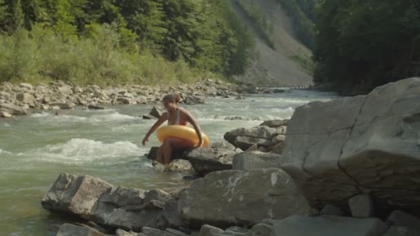 Jolie voyageuse noire insouciante en maillot de bain et anneau gonflable plongeant dans une rivière de montagne rugueuse — Video