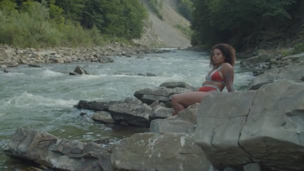 Досить африканська американка в купальнику насолоджується відпочинком і свободою в гірській річці. — стокове відео