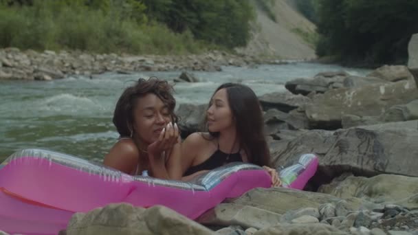 Bastante multicultural amigas en traje de baño disfrutando de ocio en colchón de aire en el río de montaña — Vídeos de Stock