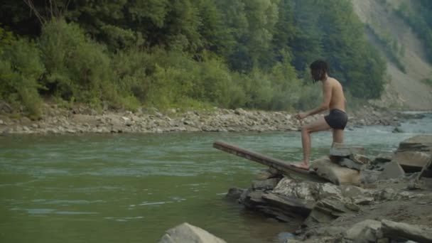 Веселый человек ныряет в горную реку с деревянного трамплина — стоковое видео