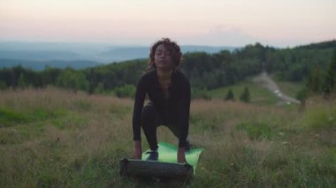 Oldukça sportif fitness Afrikalı bir kadın şafakta dağlarda hilal şeklinde poz veriyor.