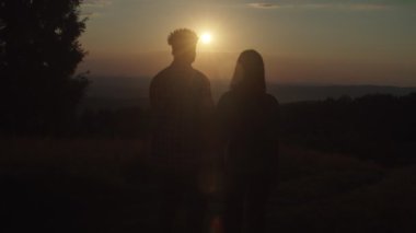 Gün batımında dağın tepesinde birbirine sarılan romantik, sevgi dolu, çok ırklı bir çift silueti.