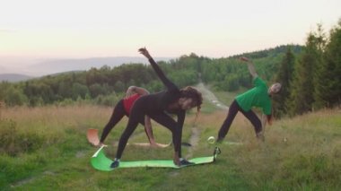 Yoga üçgeninde gerinen çok ırklı kadınlar güneş doğarken dağın tepesinde poz verirler.