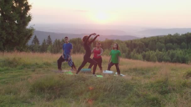 Různorodí multiraciální lidé s fitness trenér dělá jóga srpek měsíc pózovat na vrcholu hory za úsvitu — Stock video